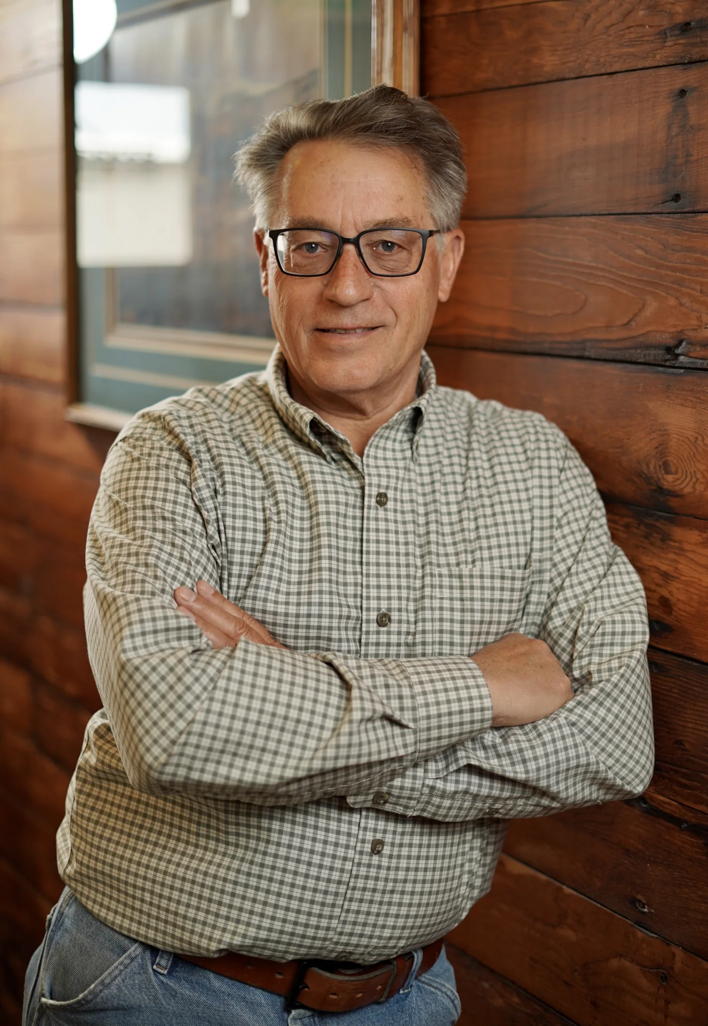 A man wearing glasses seated beside a wood-paneled wall