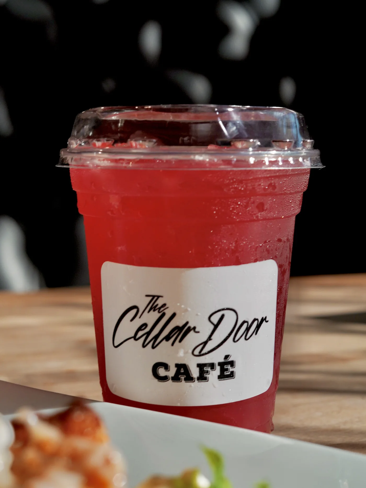 A red iced drink in a Cellar Door Café cup on a wooden table