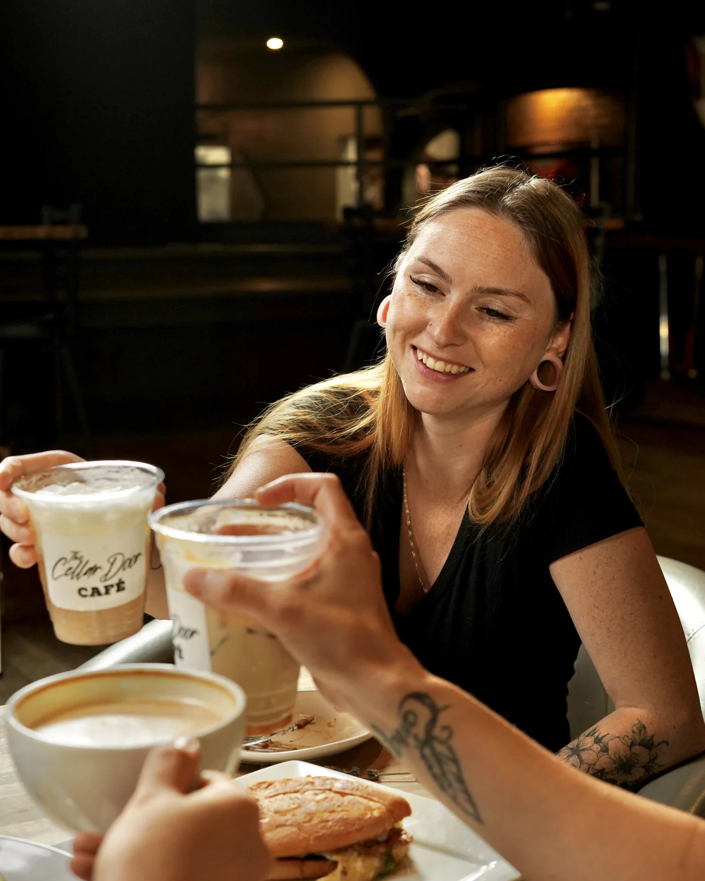 A woman smiling over coffee with friends at The Cellar Door Café
