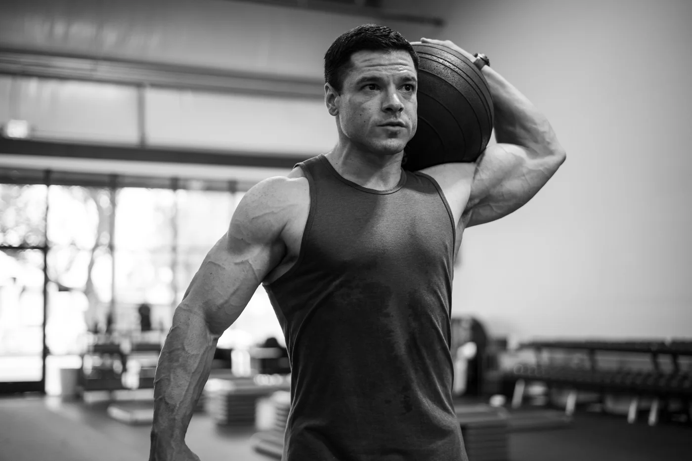 Black-and-white photograph of an athlete holding a medicine ball at his shoulder