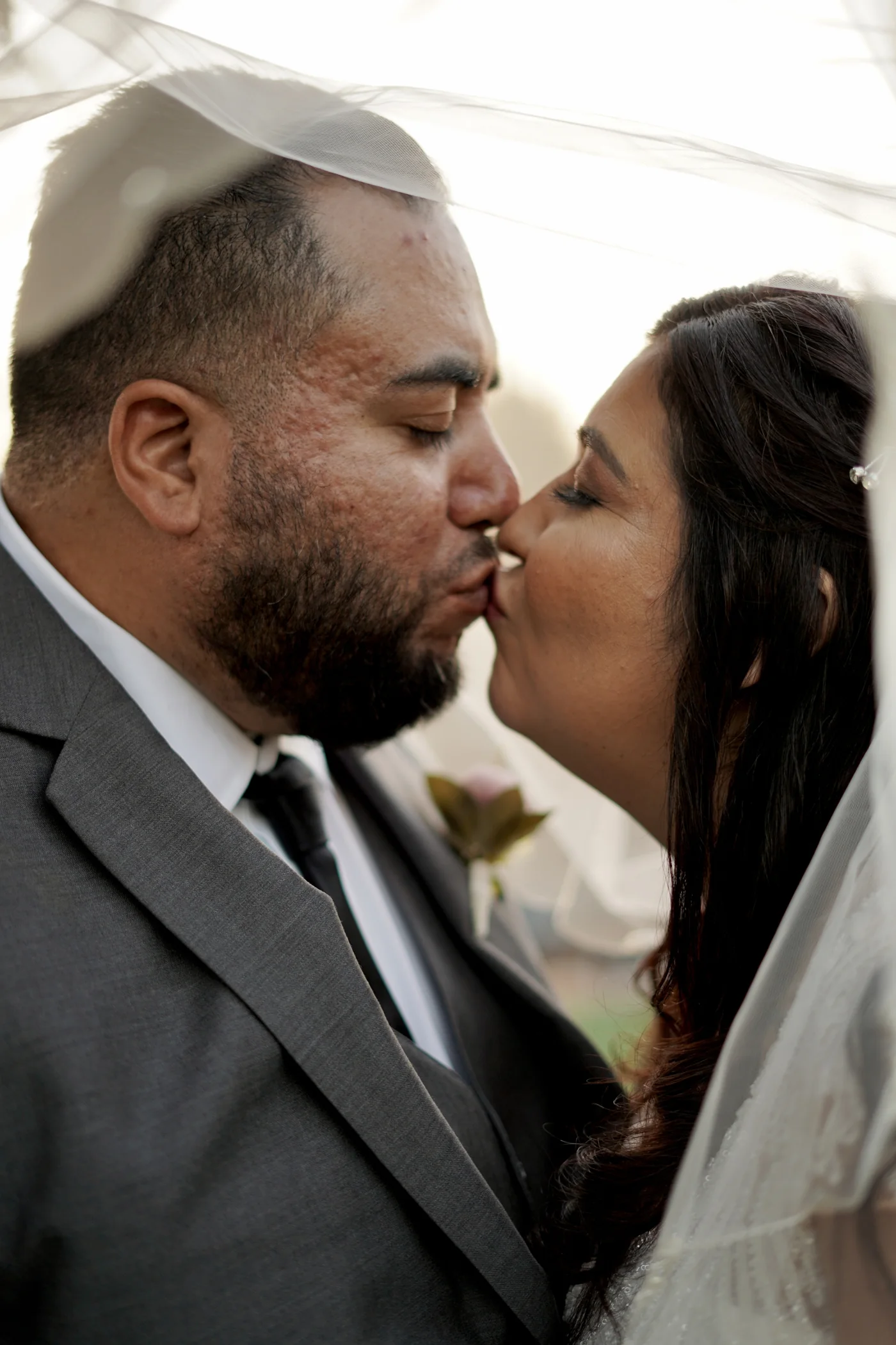 Bride and groom sharing a kiss beneath a veil